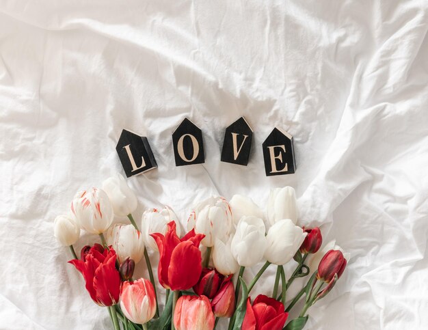 Free photo decorative word love and tulips in a white bed top view