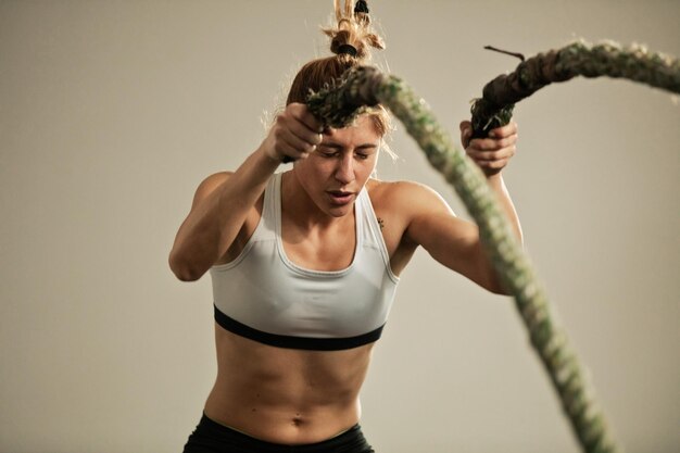 체육관에서 교차 훈련을 하고 전투 밧줄로 운동하는 헌신적인 여성 운동선수
