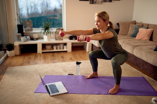 Atleta dedicata che pratica squat mentre usa i manubri a casa