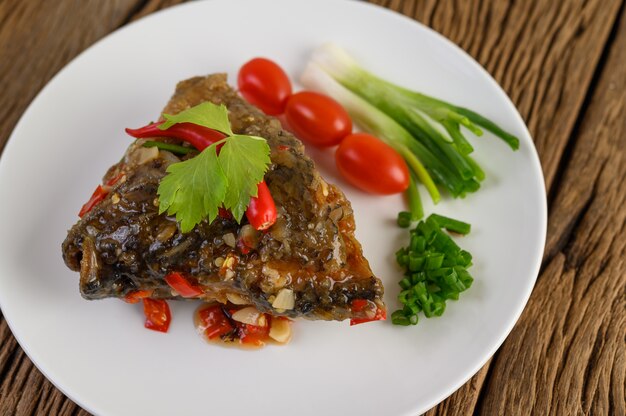 Deep-fried fish heads topped with chilies on a white plate with tomatoes and spring onions.