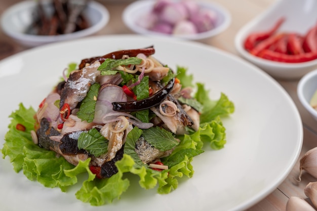 Deep-fried mackerel topped with galangal, pepper, mint, red onion in a white dish.