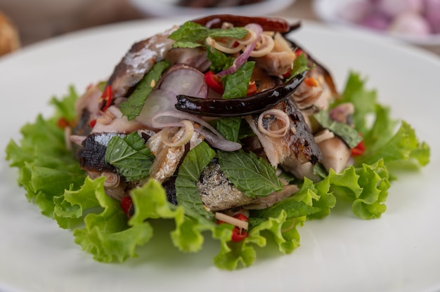 Deep-fried mackerel topped with galangal, pepper, mint, red onion in a white dish.