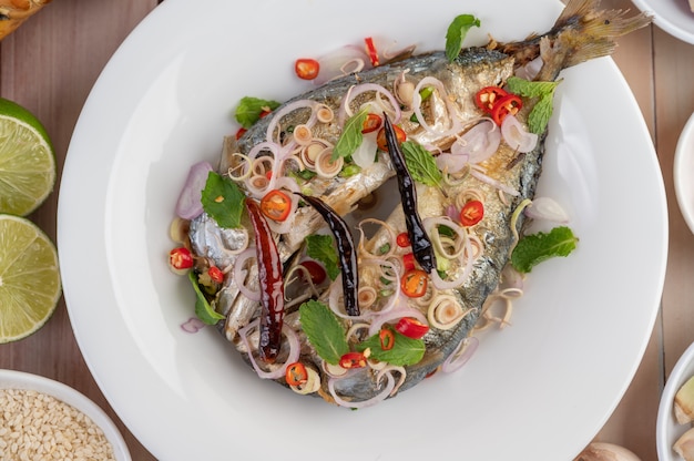 Deep-fried mackerel topped with galangal, pepper, mint, red onion in a white dish.