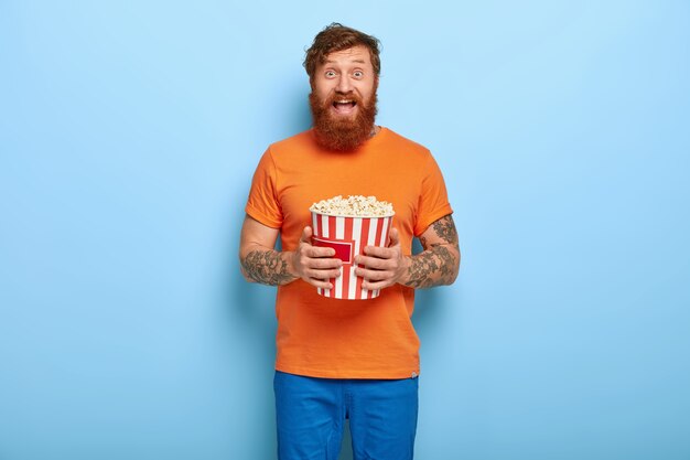 Deeply entertained bearded redhead man eats popcorn