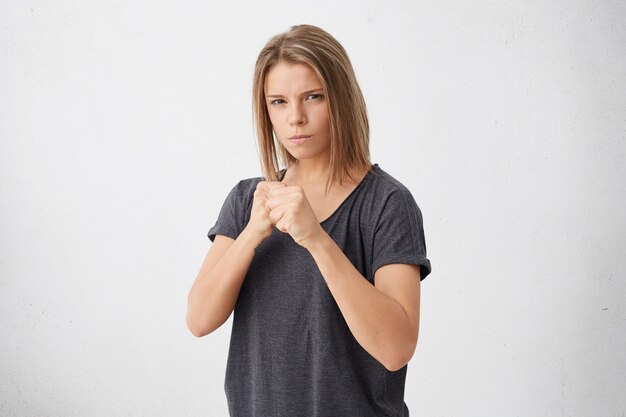 Defence and protection concept. Strong sport woman having serious and confident look keeping fists clenched in front of her defencing herself from offence and bad treatment