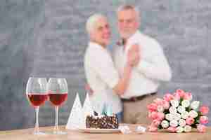 Foto gratuita coppia sfocato che balla davanti al bicchiere di vino; torta deliziosa; fiori di tulipano sul tavolo di legno