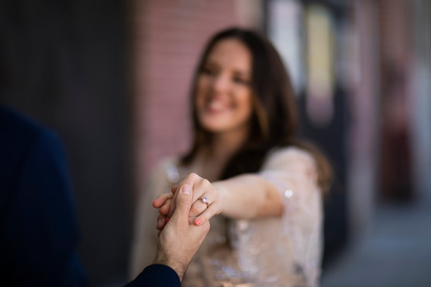 Defocused couple holding hands outdoors showing engagement ring