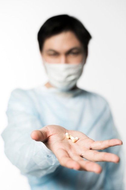 Defocused doctor with medical mask holding pills in hand