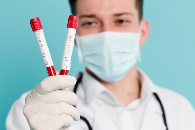 Defocused doctor with medical mask holding up vacutainers