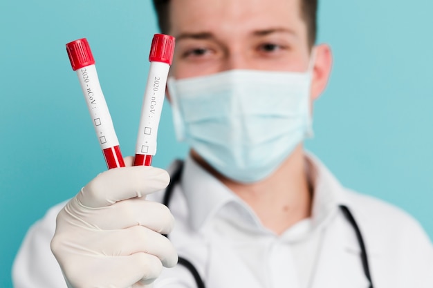 Defocused doctor with medical mask holding up vacutainers