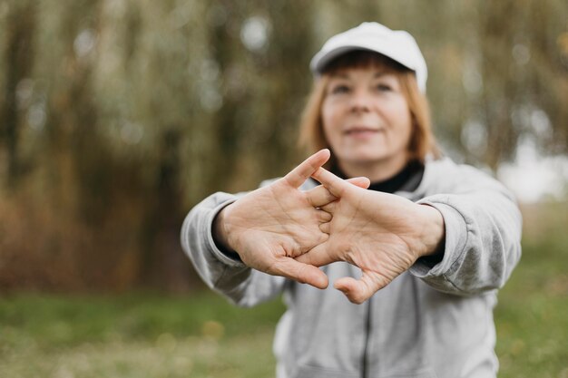 Defocused elderly woman stretching her arms outdoors