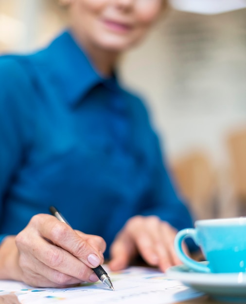 Foto gratuita donna più anziana defocused di affari che mangia caffè e che lavora sui documenti