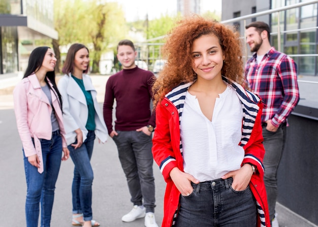 Defocused people standing behind their female friend with curly hairs looking at camera