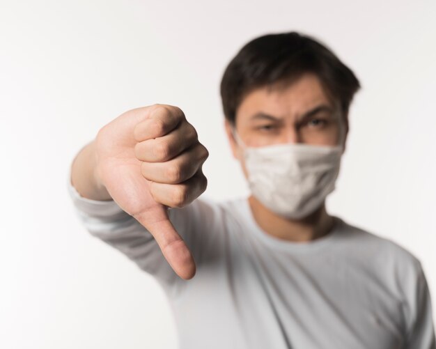 Defocused sick man with medical mask giving thumbs down