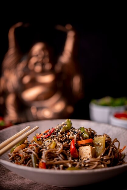 Defocused statue with bowl of noodles with vegetables