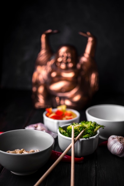 Defocused statue with cups of vegetables and chopsticks