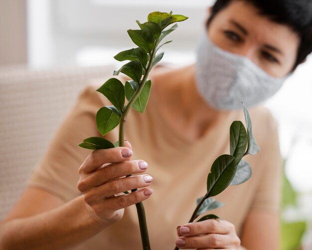 Расфокусированные женщина с маской для лица заботится о комнатных растениях