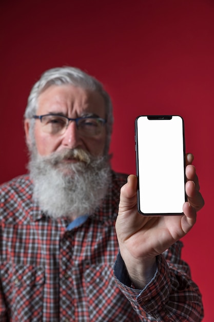 Defocussed senior man showing mobile phone with blank white screen against red background