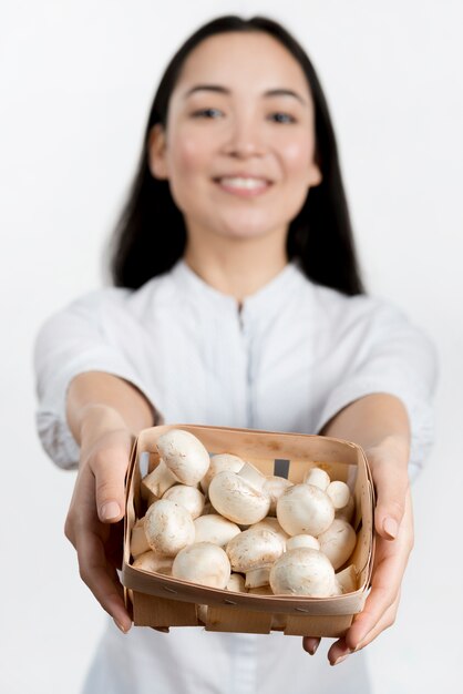 Defocussed woman showing raw mushrooms container in white background