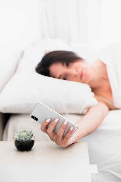 Defocussed young woman lying on bed looking at smartphone