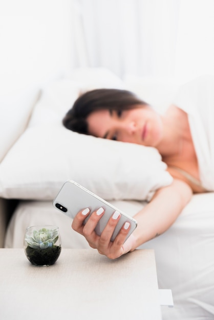 Расфокусированным молодая женщина, лежа на кровати, глядя на смартфон