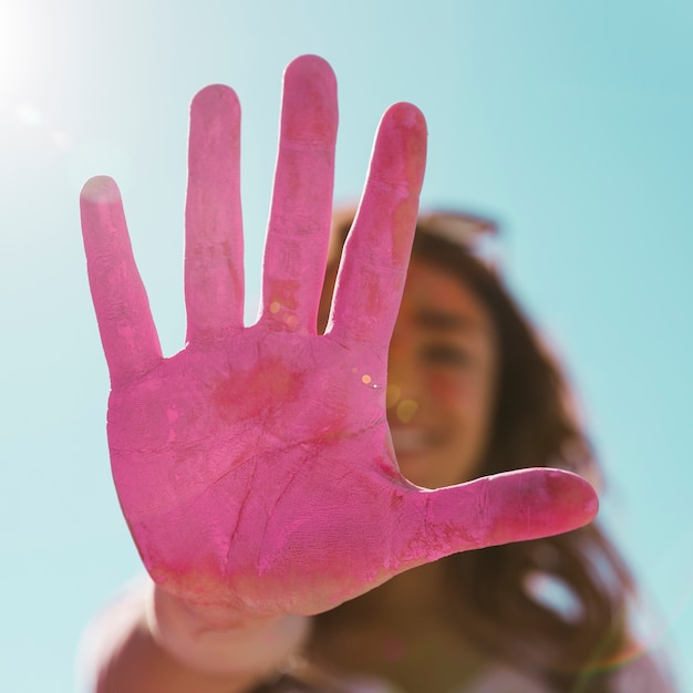 青い空を背景に日光の下で彼女の塗られたピンクのホーリー色の手を示すピンぼけの若い女性