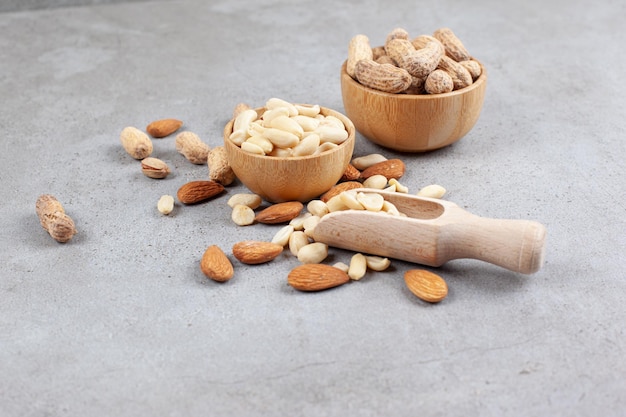 A delectable assortment of nuts in bowls and scattered next to scoop on marble surface