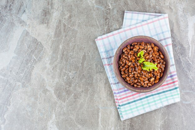 Delectable baked beans in a bowl on tea towel on marble.