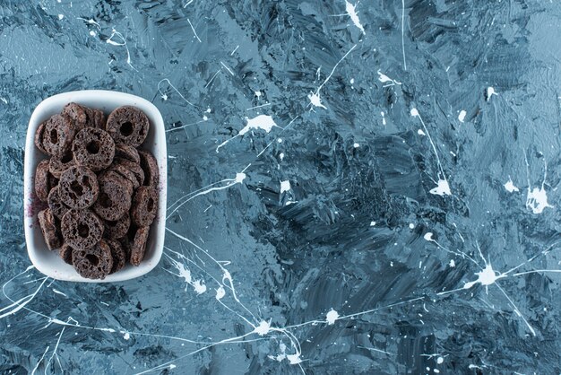 Восхитительное кольцо из кукурузы в шоколадной глазури в миске на мраморном фоне.