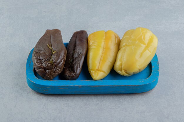 Delectable pickles eggplants and sweet peppers on the wooden plate, on the marble surface