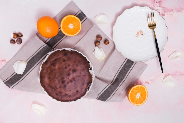 Free photo delicious baked cake; hazelnut; citrus fruits and white petals on textured background