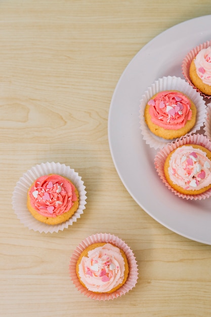 Delicious beautiful cupcakes on plate and wooden surface