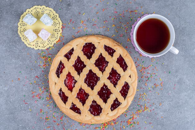 Delicious berry pie, candies and tea on marble surface