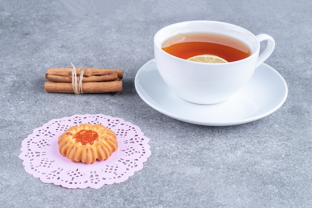 Delicious biscuit, cup of tea and cinnamon sticks on marble surface