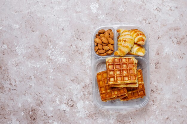 アーモンド、赤いリンゴのスライス、ワッフル、光の上のプラスチック製のランチボックスにクロワッサンとおいしい朝食