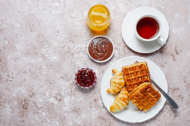 コーヒー、オレンジジュース、ワッフル、クロワッサン、ジャム、ナッツペーストの光、トップビューで美味しい朝食