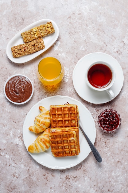 Delicious breakfast with coffee, orange juice, waffles,croissants,jam,nut paste on light ,top view