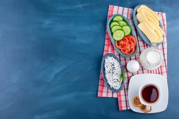 Delicious breakfast with tea, milk and cheese on blue surface. 