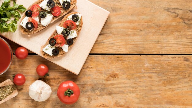 Delicious bruschetta on wooden cutting board and ingredient over wooden desk