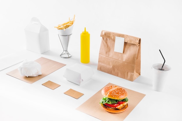 Foto gratuita hamburger delizioso; pacchi; tazza di smaltimento e bottiglia di salsa su sfondo bianco