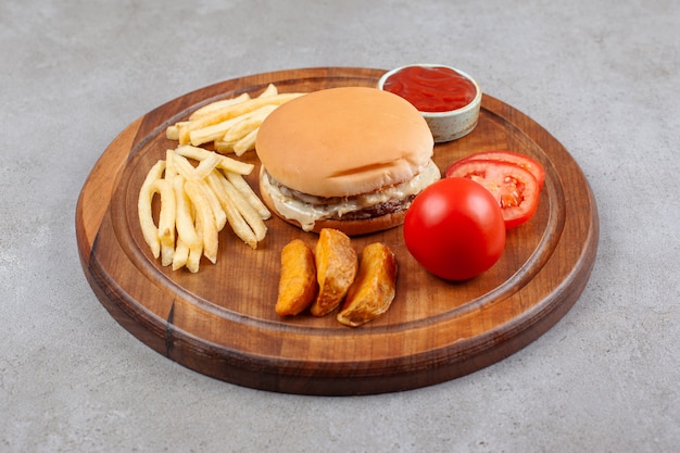 Delicious burger with potato fries and ketchup on wooden board