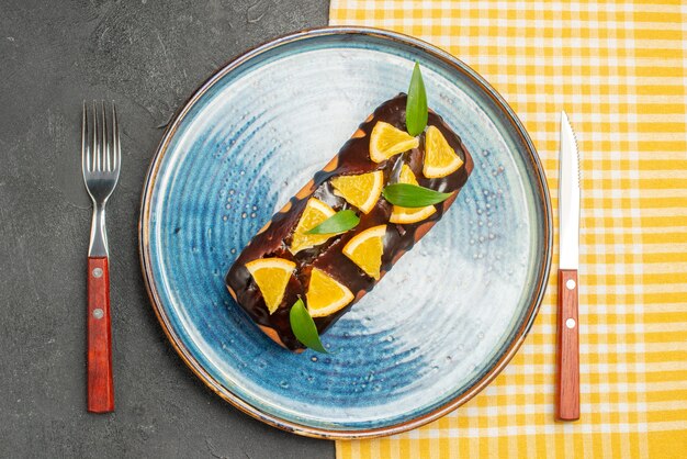 Foto gratuita deliziosa torta decorata con arancia e cioccolato servita con forchetta e coltello sul tavolo scuro