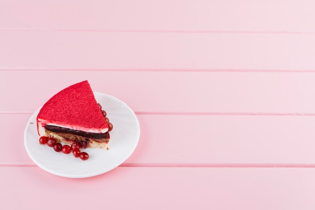 Free photo delicious cake slice with red currant berries on white plate over the pink plank backdrop