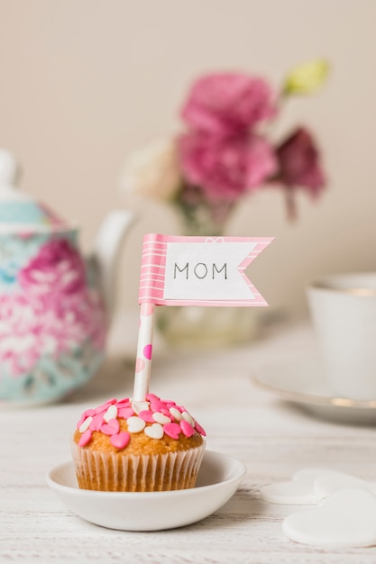 Вкусный торт с декоративным флагом с названием мамы рядом с чайником и цветами