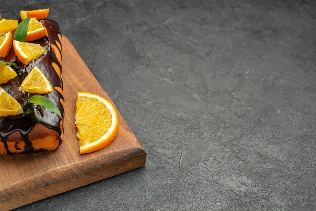 Delicious cakes decorated with orange and chocolate on cutting board on black table