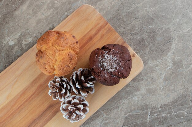 Delicious cakes with pinecones on wooden board