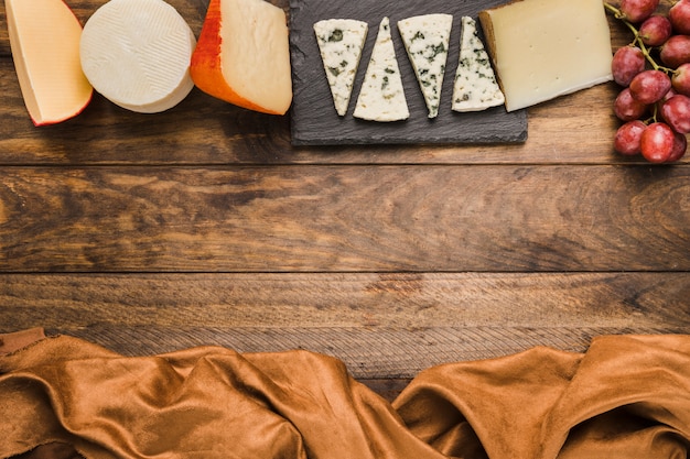 Бесплатное фото Вкусный сыр и виноград расположены в ряд на деревянном столе с коричневой тканью
