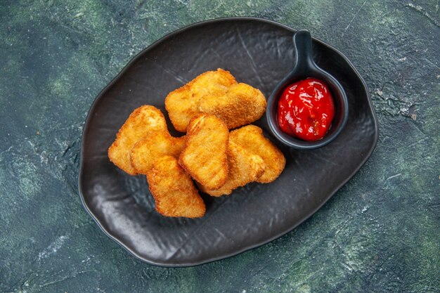 Delicious chicken nuggets and ketchup in black plates on dark surface with free space in close up shot