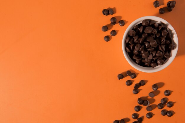 Delicious chocolate chips in bowl flat lay