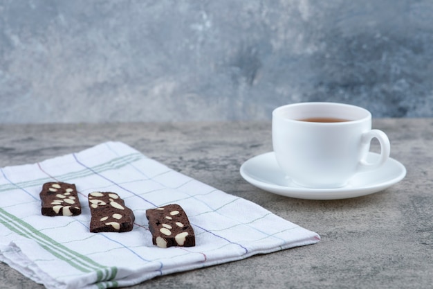 Deliziose fette biscottate di pane al cacao con noci e tazza di tè aromatico sulla superficie in marmo.